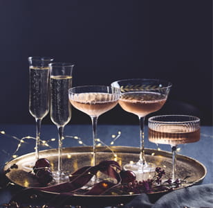 A selection of different filled wine glasses on a gold tray with festive ribbon and decorations on a dark blue background